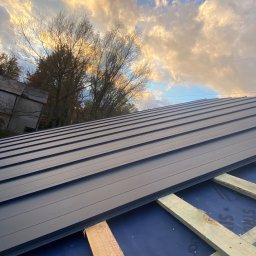 ND-BUD Nazarii Doroshchuk - Montaż blachy na dachu z widocznymi łatami i membraną dachową, na tle zachmurzonego nieba i drzew.