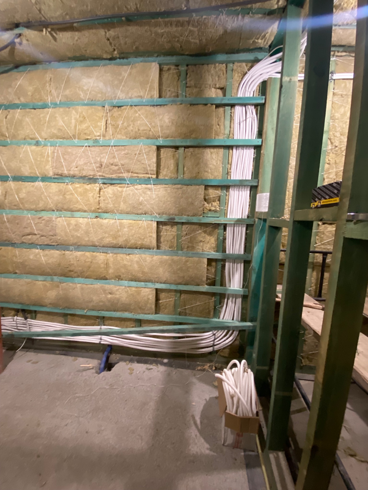 Wnętrze w trakcie prac: wełna mineralna między drewnianymi belkami, zabezpieczona sznurkiem, oraz wiązki przewodów elektrycznych w białej izolacji, ułożone wzdłuż ramy.