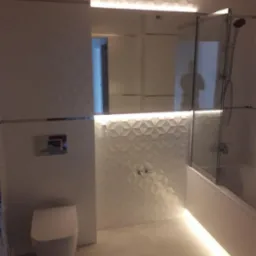 Nowoczesna łazienka z podświetleniem LED pod sufitem i wanną, biała armatura i geometryczna tekstura płytek na ścianie.