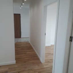 Rem-Instal Michał Laskowski - Korytarz po remoncie z drewnianą podłogą, białymi ścianami i nowym oświetleniem punktowym na suficie.