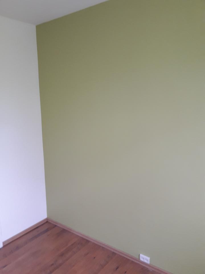 Pomieszczenie po malowaniu ścian na odcień oliwkowej zieleni, widoczna ściana pomalowana na zielono i fragment ściany pomalowanej na biało, drewniana podłoga oraz listwa przypodłogowa.