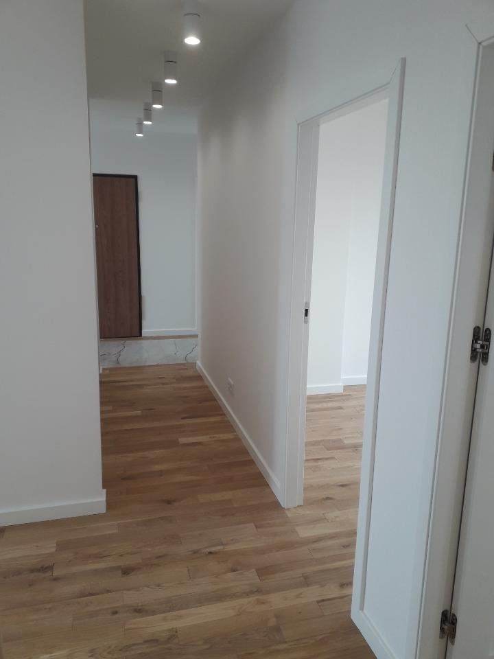 Korytarz po remoncie z drewnianą podłogą, białymi ścianami i nowym oświetleniem punktowym na suficie.