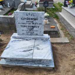 Emilia Tomaszewska - Jasnoszary nagrobek z inskrypcjami na cmentarzu, otoczony innymi grobami. Widoczne kwiaty i znicze. Ujęcie z bliska, z ziemią w dolnej części kadru.