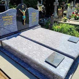 Emilia Tomaszewska - Granitowy nagrobek podwójny z rzeźbą Jezusa na cmentarzu. Jasnoszary kamień z ciemnymi żyłkami, inskrypcje na tablicach. W tle inne groby i zieleń.