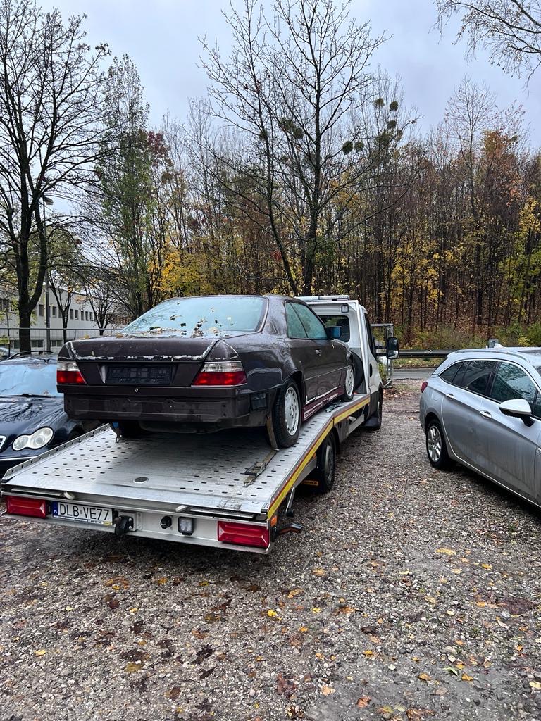 Brązowy, uszkodzony samochód osobowy na platformie lawety, widok z tyłu, jesienne otoczenie.