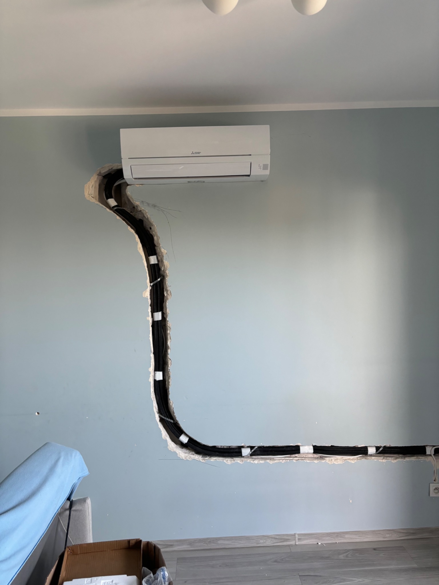 Montaż klimatyzacji w domu: widoczny klimatyzator Mitsubishi Electric na ścianie z wyciętym bruzdą na rurę chłodniczą, zabezpieczoną taśmą, przed dalszymi pracami wykończeniowymi.