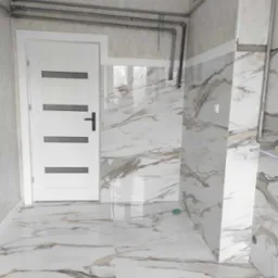 Wykończona łazienka z marmurowymi płytkami na ścianach i podłodze, białe drzwi z poziomymi szarymi paskami, widoczne rury pod sufitem.