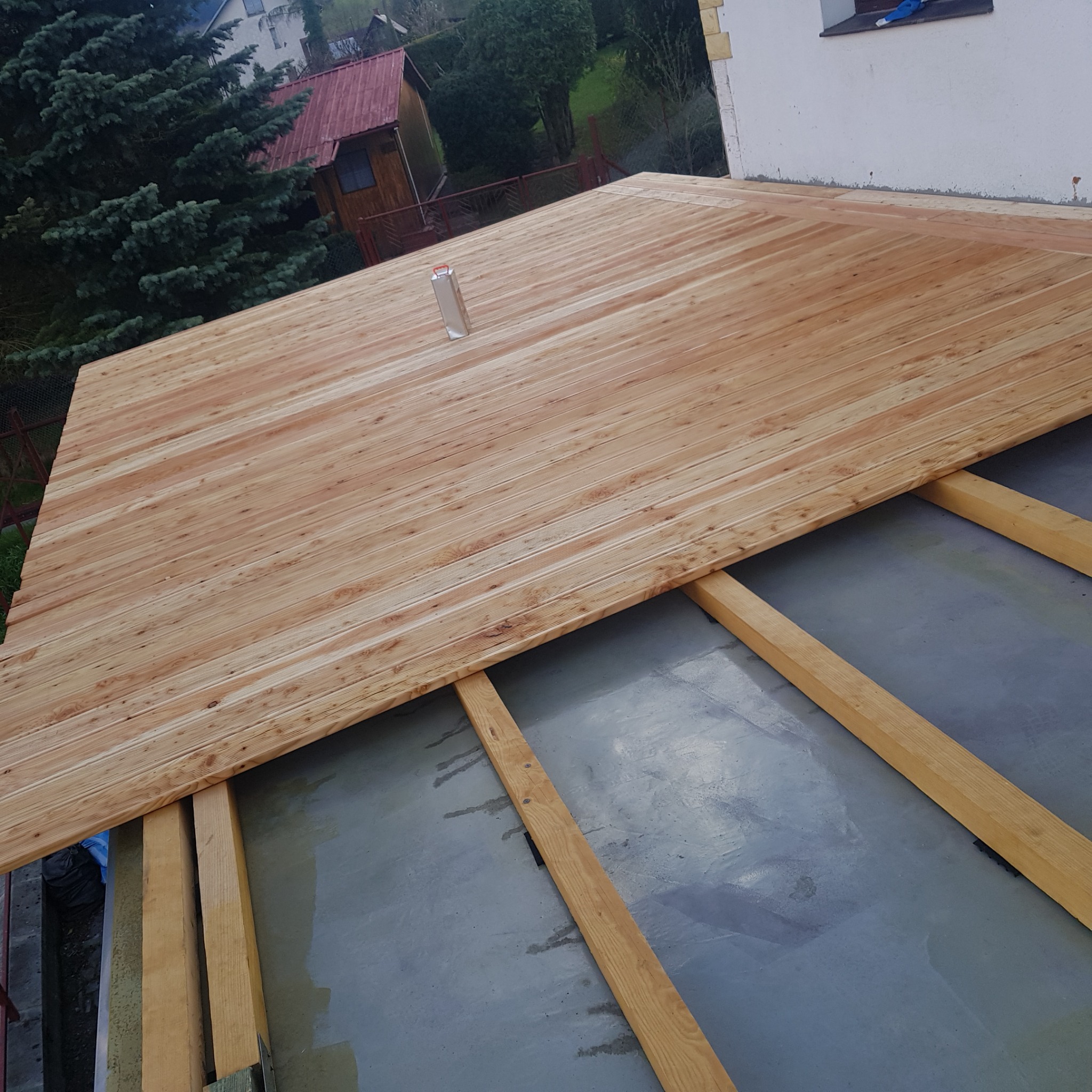 Montaż drewnianej podłogi na legarach z widocznymi deskami i podłożem, butelka po napoju na powierzchni podłogi.