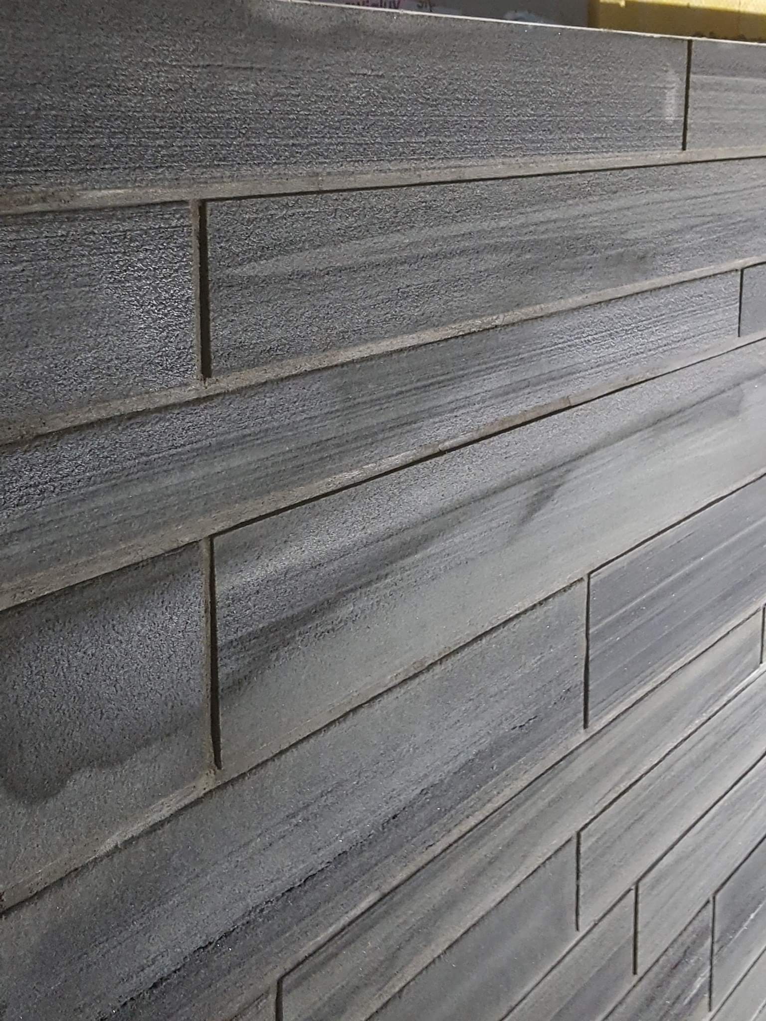 Ściana wyłożona szarymi, drewnopodobnymi panelami z wyraźną fakturą i fugami, ułożonymi poziomo, widziana pod kątem.
