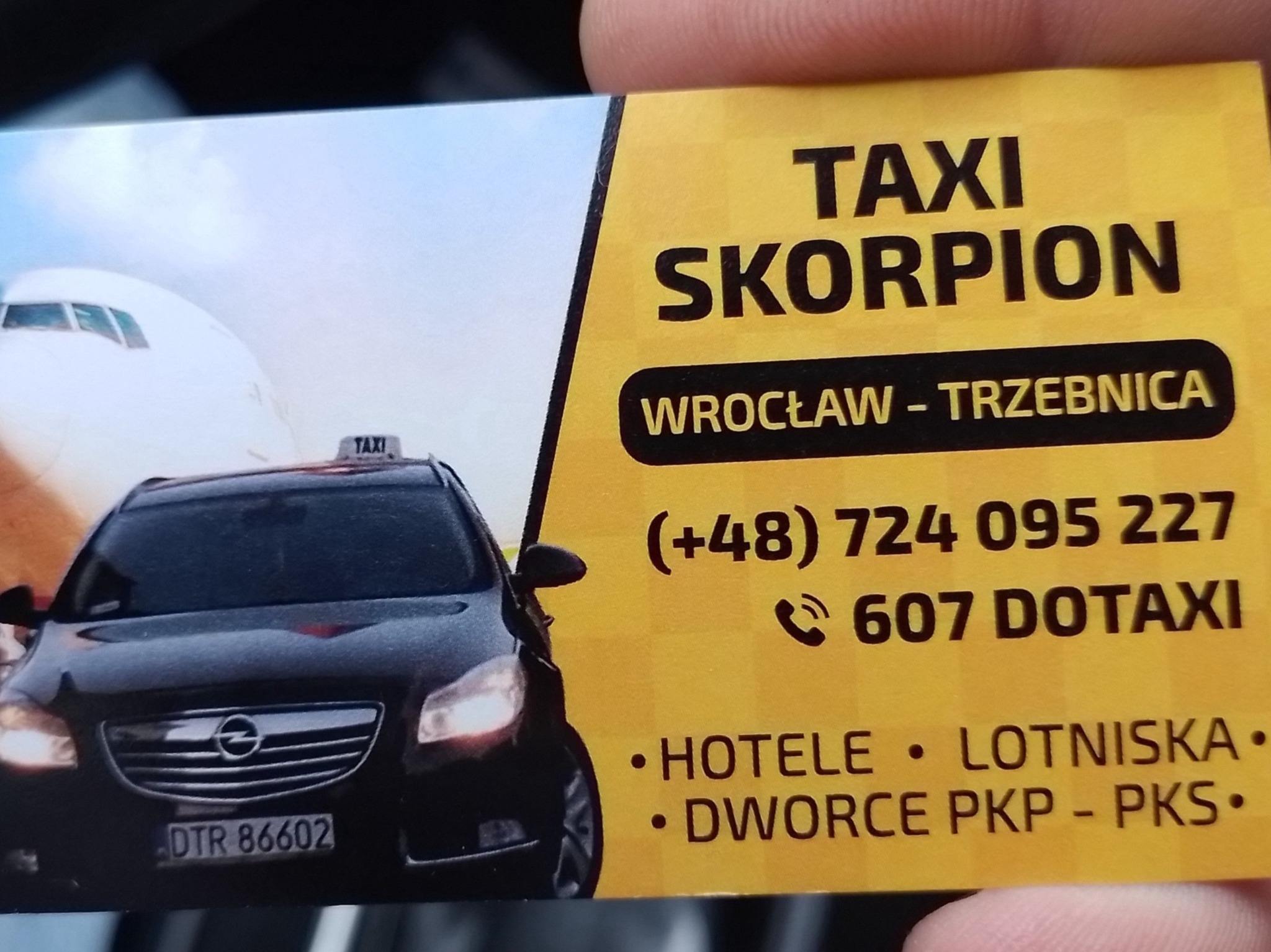 Wizytówka Taxi Skorpion z Wrocławia i Trzebnicy, z czarnym samochodem i samolotem w tle, numer telefonu i informacja o obsłudze hoteli, lotnisk i dworców.