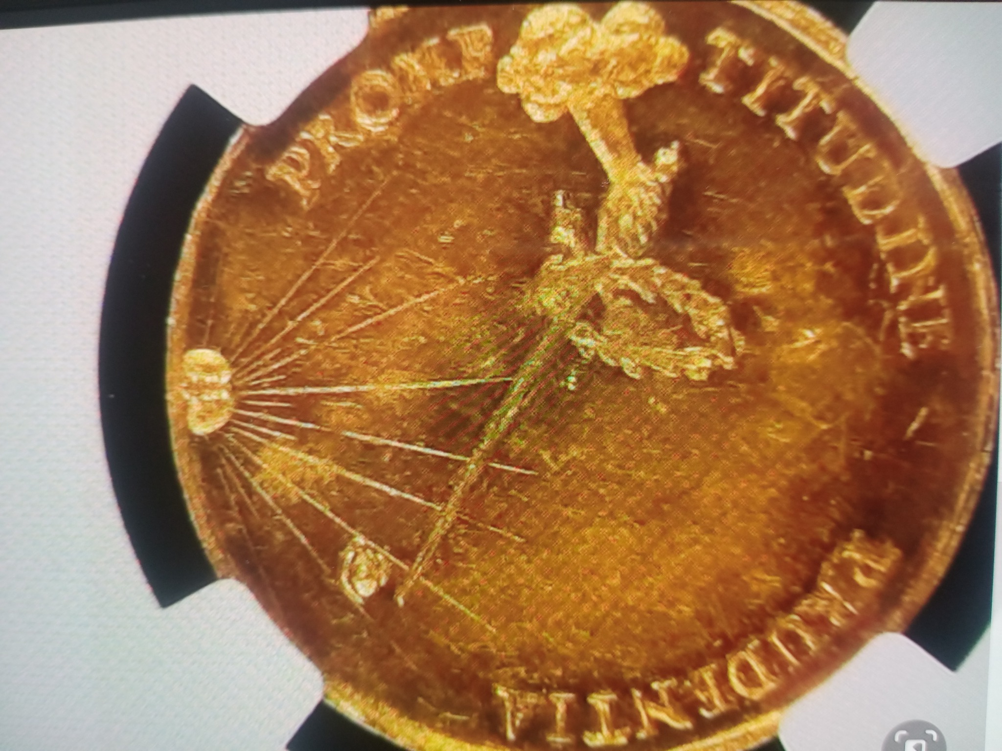 Złota moneta z inskrypcjami 'PRUDENTIA' i 'PROMITUDINE' umieszczona w ochronnej obudowie.