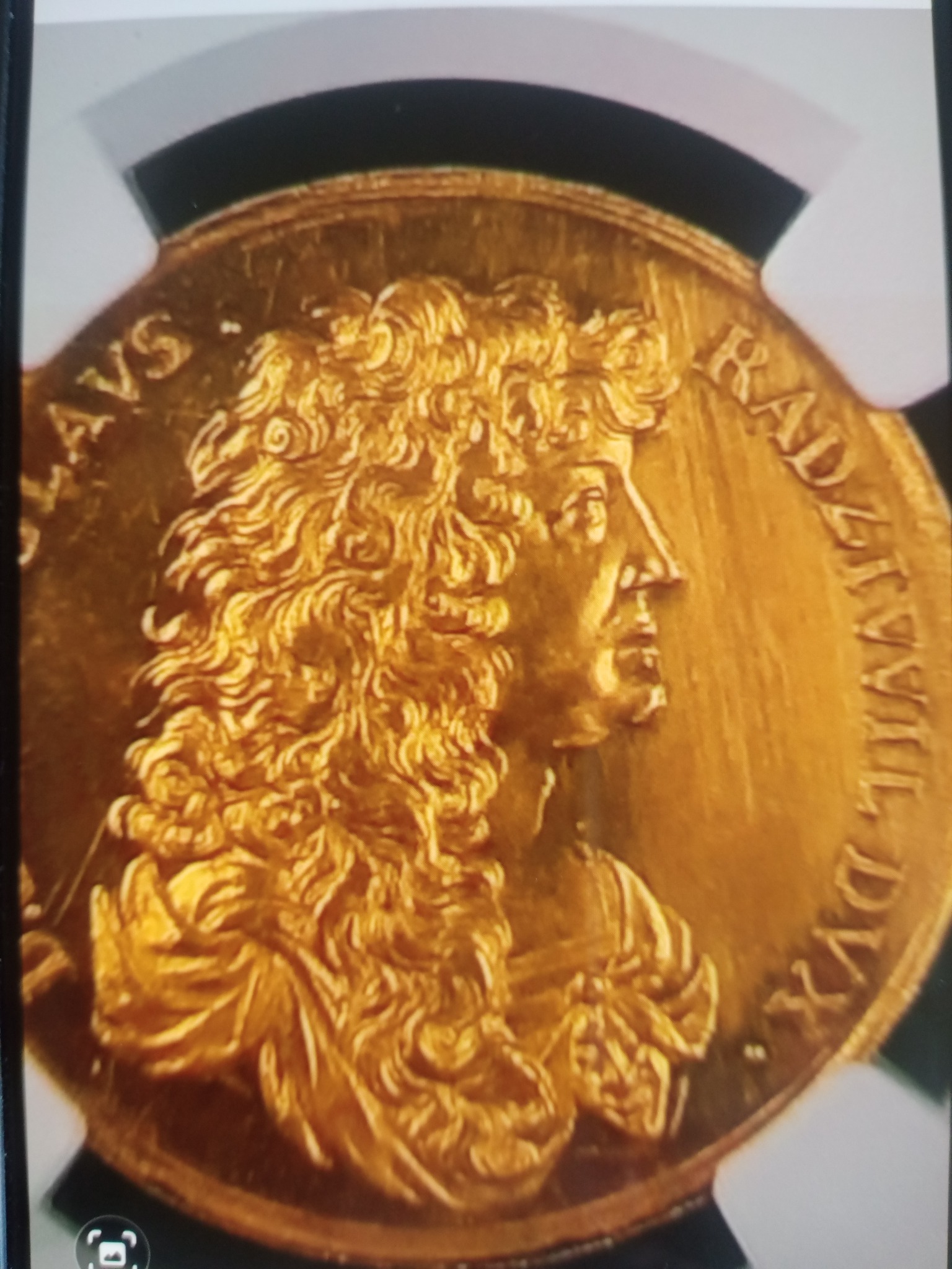 Złota moneta kolekcjonerska z wizerunkiem mężczyzny w peruce, otoczona inskrypcjami, umieszczona w ochronnym etui.