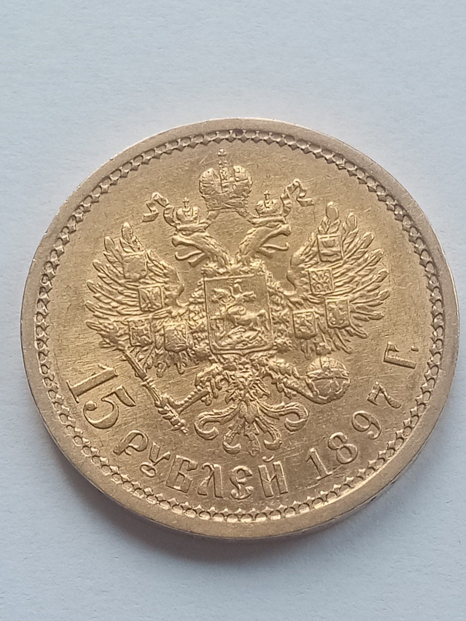 Złota moneta rosyjska o nominale 15 rubli z 1897 roku, z wizerunkiem dwugłowego orła carskiego na awersie.