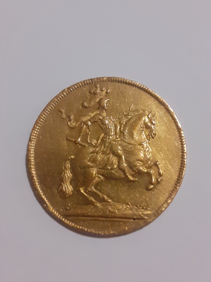 Złota moneta z wizerunkiem jeźdźca na koniu, widoczna z bliska, z detalami reliefu.