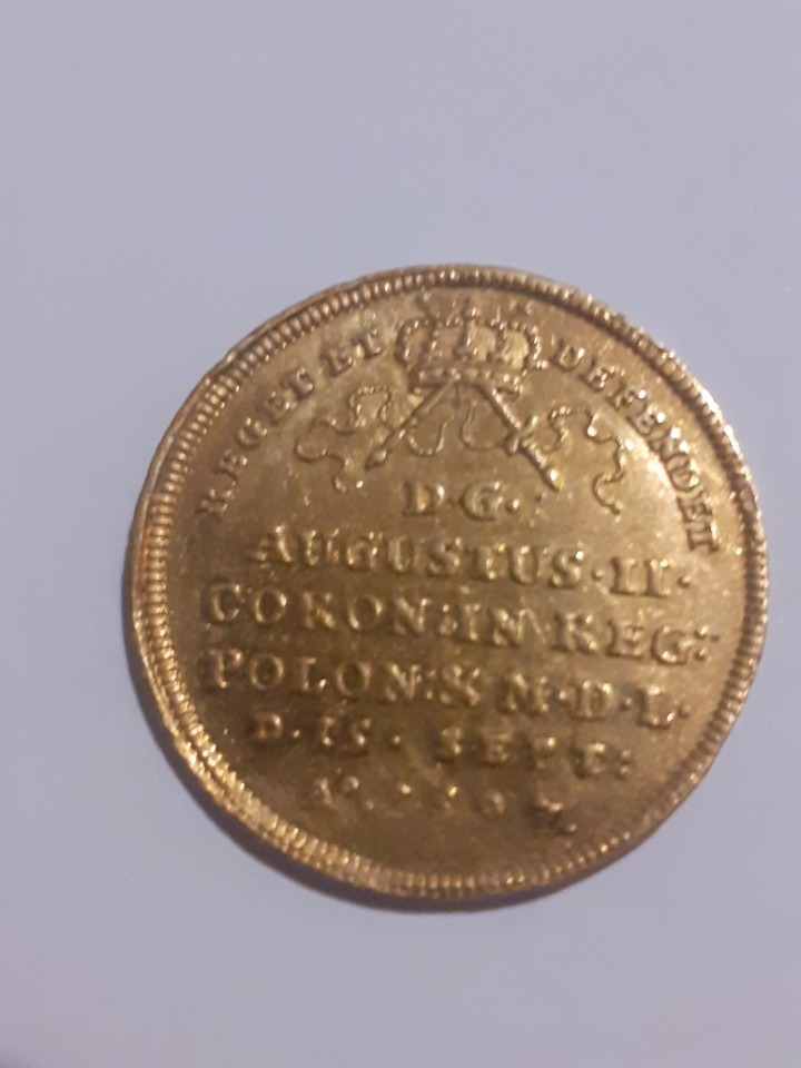 Złota moneta Augusta II Mocnego, prawdopodobnie znaleziona w okolicach Białegostoku, z inskrypcjami łacińskimi i koroną. Widoczne detale wytłoczeń i delikatna patyna.