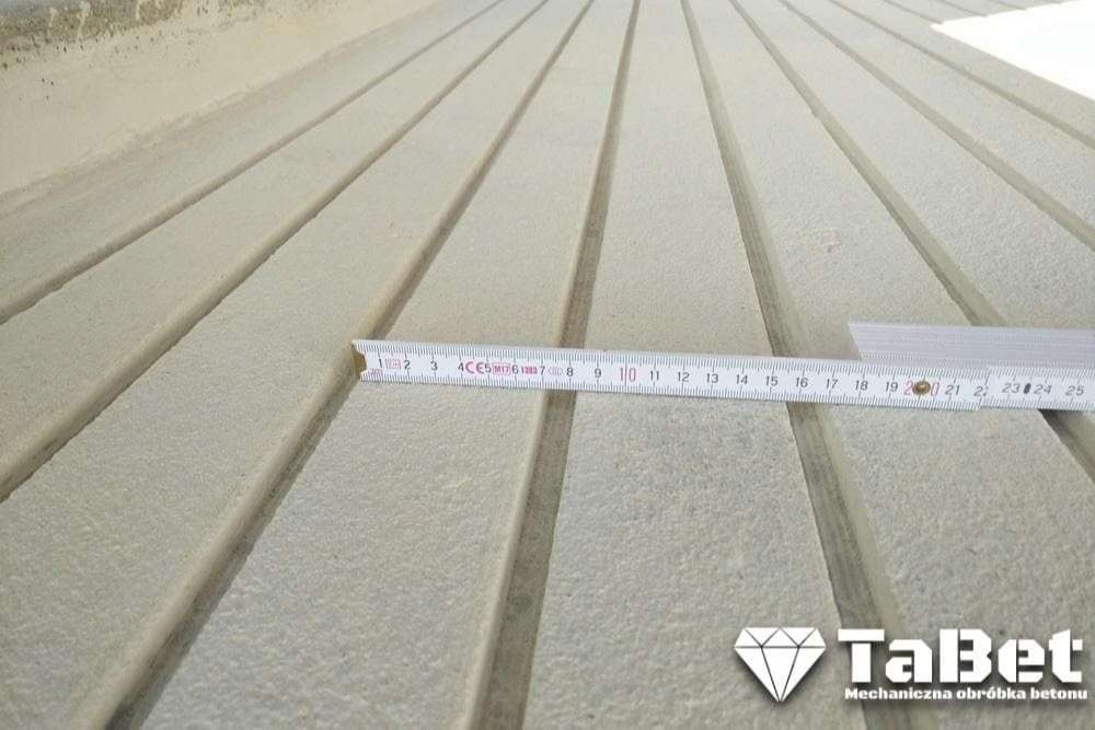 Nacięta posadzka betonowa z rowkami, pomiar szerokości rowka za pomocą rozłożonej miarki, widoczne logo firmy TaBet zajmującej się mechaniczną obróbką betonu.