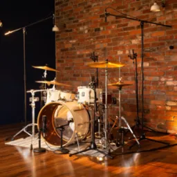 Profesjonalnie oświetlony zestaw perkusyjny z mikrofonami w studiu nagrań, z ceglaną ścianą w tle i drewnianą podłogą.