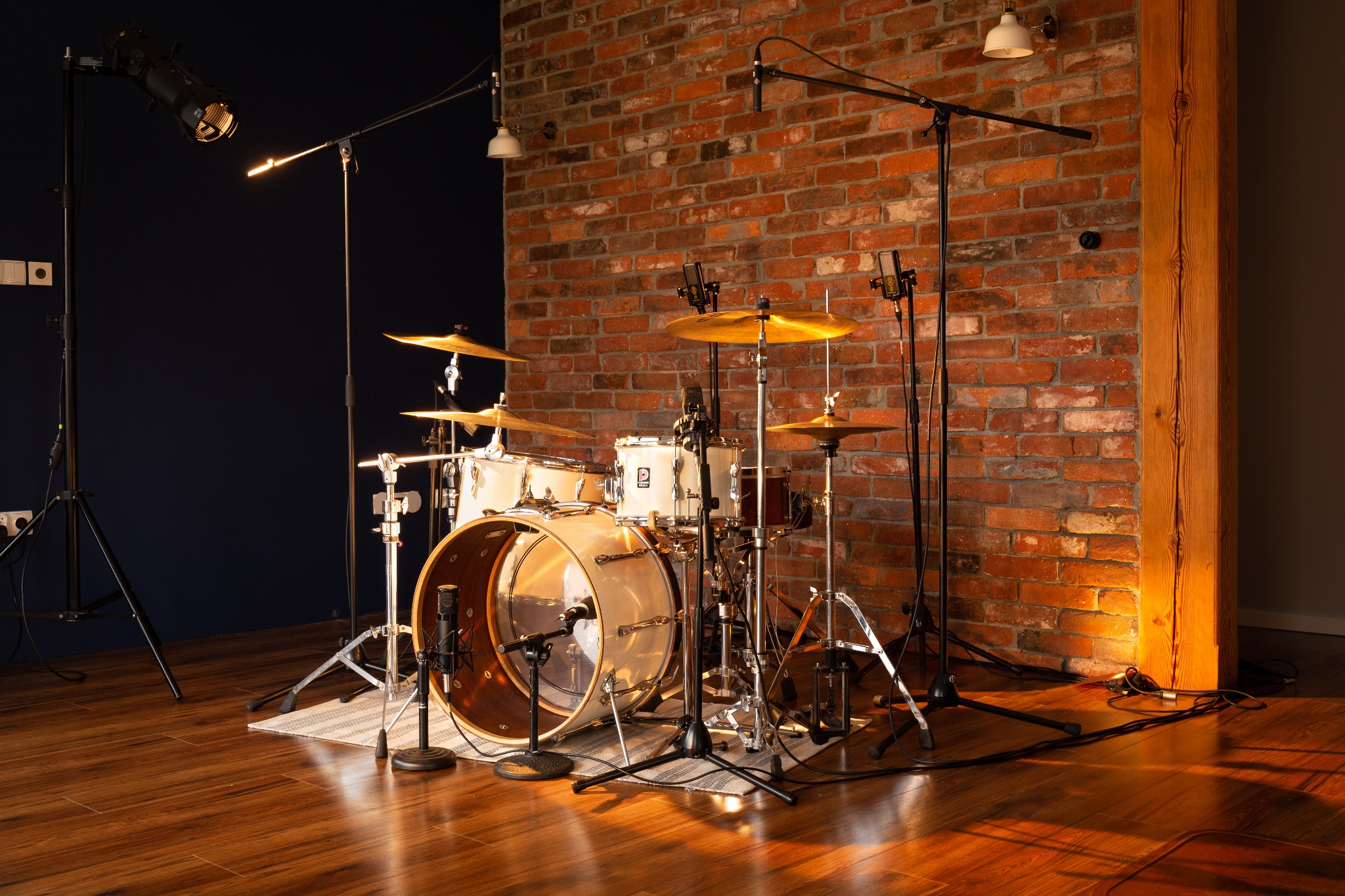 Profesjonalnie oświetlony zestaw perkusyjny z mikrofonami w studiu nagrań, z ceglaną ścianą w tle i drewnianą podłogą.
