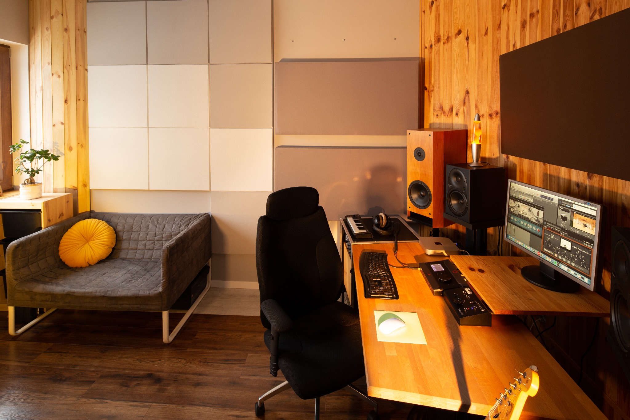Profesjonalne studio nagrań z drewnianymi panelami ściennymi, akustycznymi panelami, biurkiem z monitorem, klawiaturą, kontrolerem MIDI, gitarą i wygodnym fotelem biurowym.