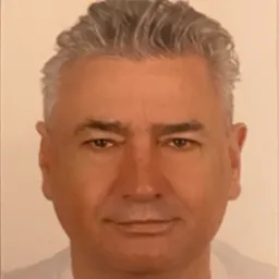 Portret mężczyzny o siwych włosach, patrzącego prosto w obiektyw z delikatnym uśmiechem.