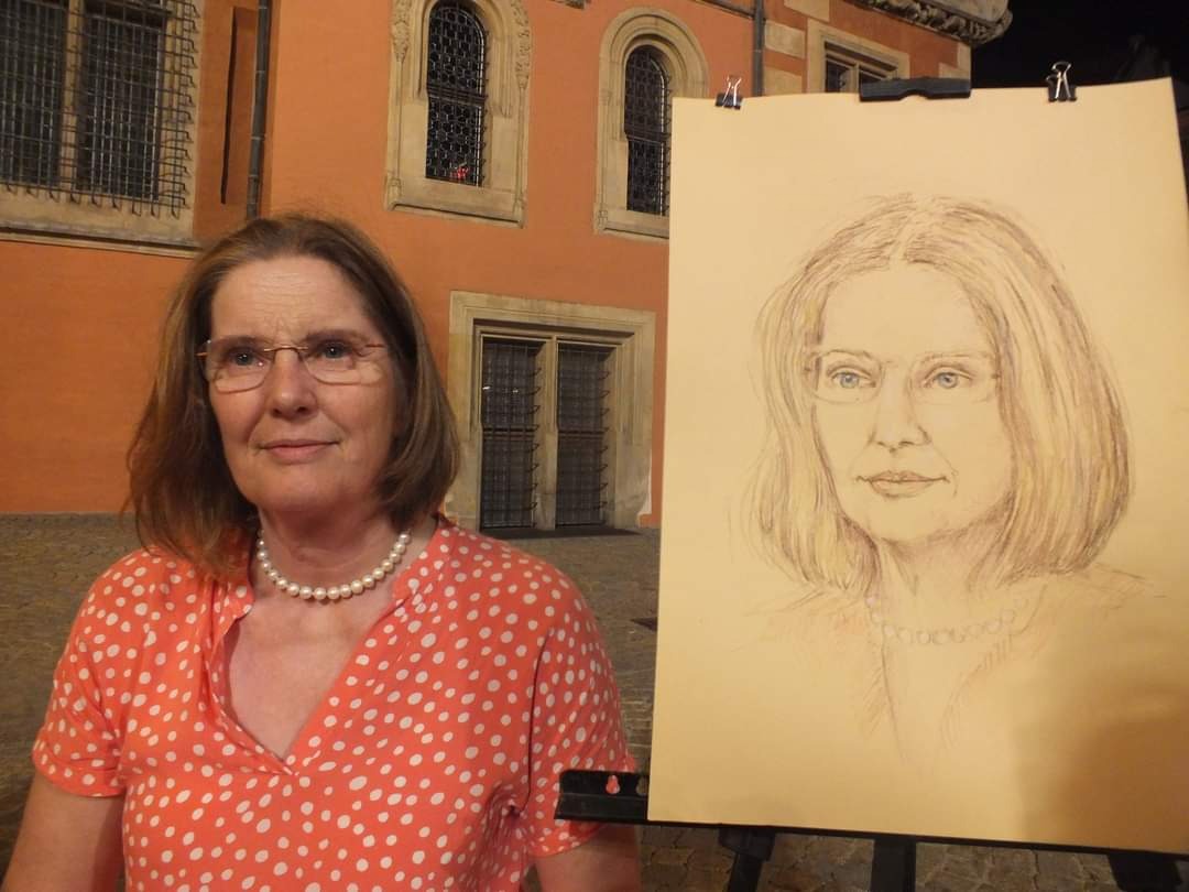 Portret kobiety wykonany ołówkiem, prezentowany obok modelki na tle budynku z oknami.