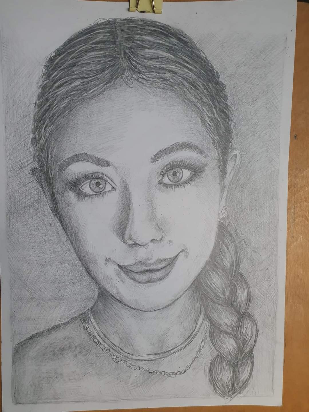 Szkic ołówkiem portretu młodej kobiety z warkoczem, na białym papierze z metalowym klipsem u góry.