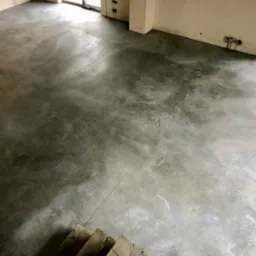 Szara, gładka posadzka z widocznymi dylatacjami w nowym budynku w Gliwicach, z fragmentem schodów w rogu kadru i niedokończonymi instalacjami elektrycznymi na ścianie.