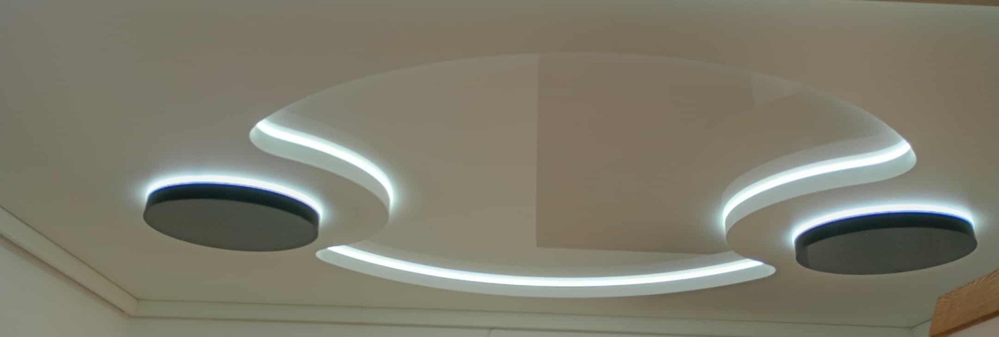 Biały sufit napinany z okrągłym wzorem i podświetleniem LED, widok z dołu. Nowoczesny design z elementami dekoracyjnymi i oświetleniem punktowym.