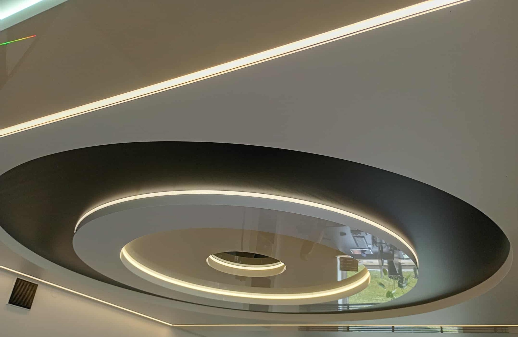 Nowoczesny sufit napinany z okrągłym wzorem i oświetleniem LED. Czarno-biała kolorystyka, gładka powierzchnia, widoczne odbicie w centralnej części sufitu.