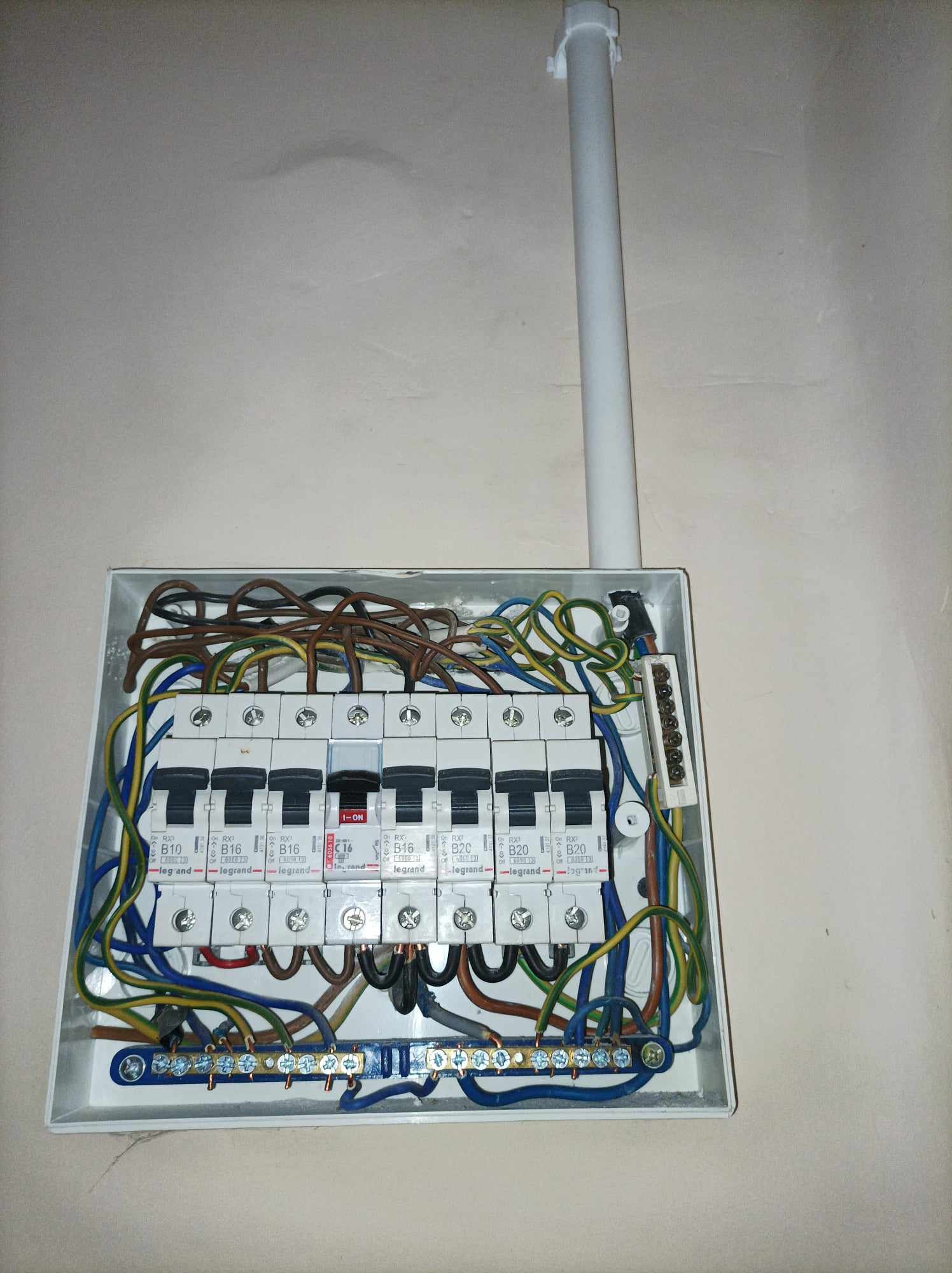 Otwarta skrzynka rozdzielcza z widocznymi bezpiecznikami Legrand B10, B16, C16 i B20, z przewodami w kolorach brązowym, niebieskim, żółto-zielonym, oraz z szyną uziemiającą, zamontowana na jasnej...