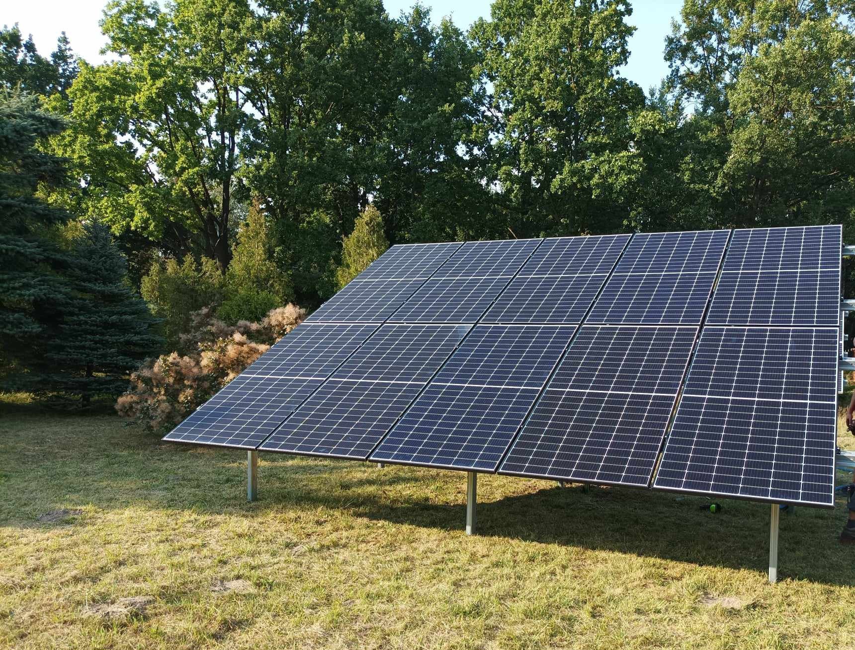 Panel słoneczny zamontowany na metalowych wspornikach na trawniku, w tle drzewa.