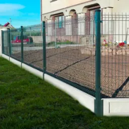 Nowoczesne, zielone ogrodzenie panelowe z podmurówką betonową, widok z zewnątrz posesji na tle domu z oknami i ogródkiem kwiatowym, zaparkowany samochód przy ulicy.