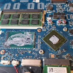 Otwarta obudowa laptopa z widoczną płytą główną, procesorem z nałożoną pastą termoprzewodzącą, modułem RAM Kingston i kartą WiFi, ukazująca skomplikowane układy elektroniczne.