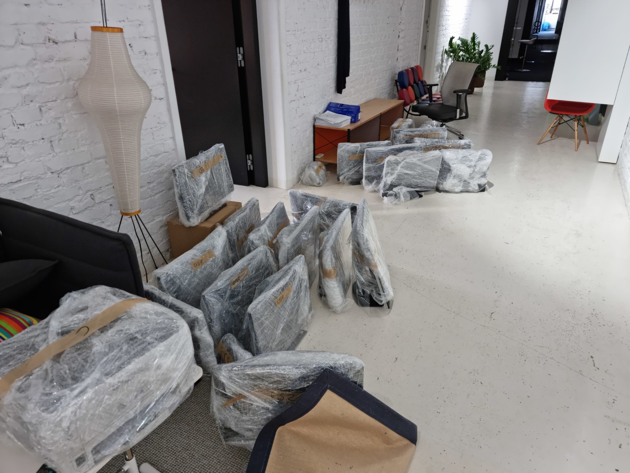 Monitory komputerowe i inne przedmioty, owinięte folią, przygotowane do transportu w pomieszczeniu z białymi ścianami i podłogą.