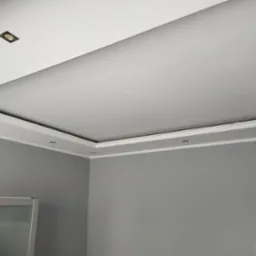 Szare ściany i biały sufit z podwieszaną częścią centralną i ozdobnymi listwami przysufitowymi oraz punktowym oświetleniem LED.