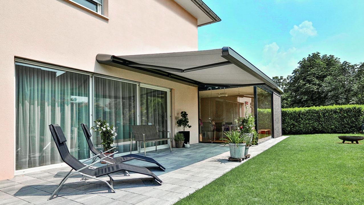 Rozłożona markiza tarasowa w kolorze szarym, chroniąca przed słońcem. Widoczne leżaki, patio i zadbany trawnik. Nowoczesny design i funkcjonalność.