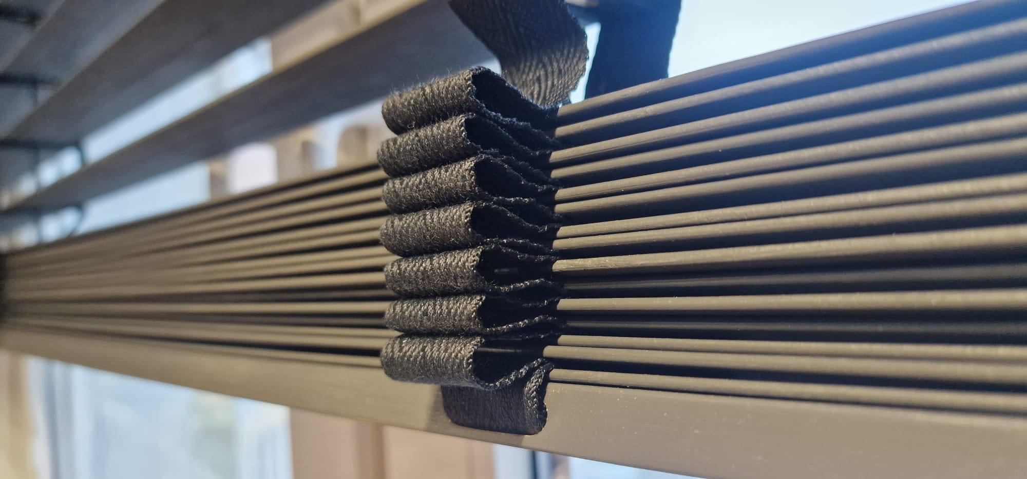 Szczegółowe ujęcie żaluzji bambusowych 50mm w kolorze grafitowym, z widocznym mechanizmem podnoszenia z ciemnej taśmy. Delikatne światło podkreśla teksturę materiału.