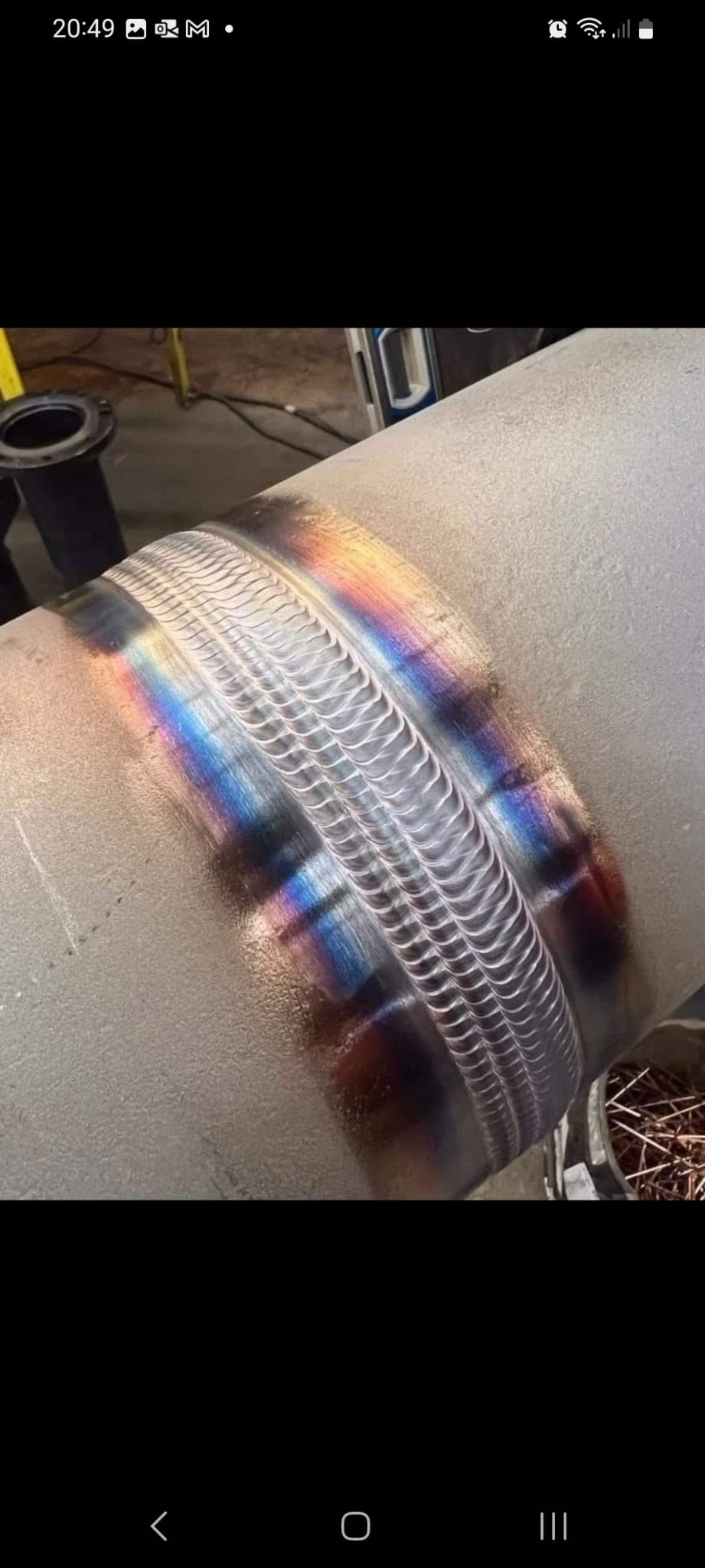 Precyzyjne spawy na metalowej rurze, widoczne tęczowe przebarwienia termiczne i regularny wzór spoin.