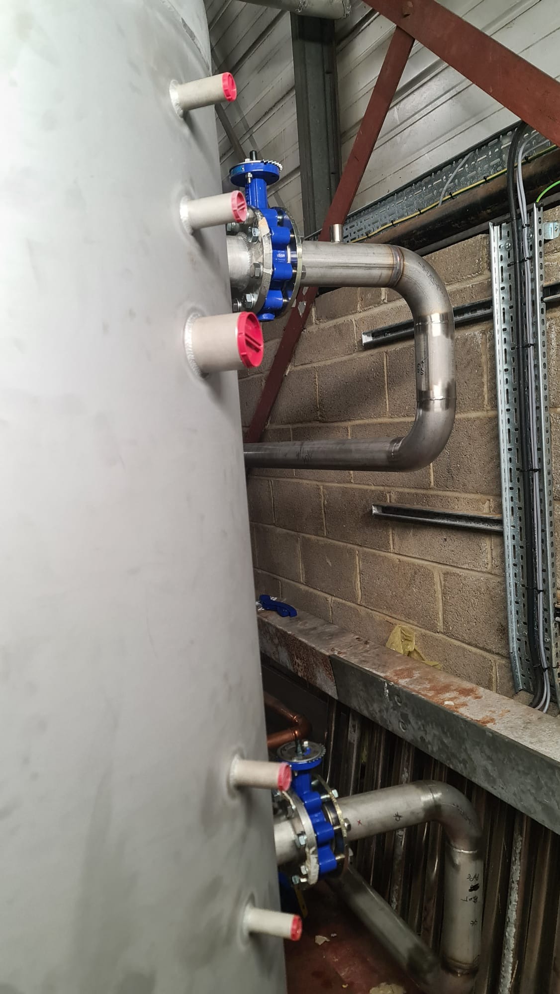 Instalacja przemysłowa w Czechowice-Dziedzice z dużym zbiornikiem, rurami ze stali nierdzewnej, zaworami z niebieskimi kołnierzami i czerwonymi zaślepkami, zamontowana przy ścianie z cegły.