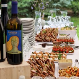 Chefs Catering - Stół cateringowy na zewnątrz: kanapki z ciemnego pieczywa, mini tartaletki z kremem i szparagami, koreczki z pomidorkami cherry i mozarellą, sałatka, frytki z warzyw korzeniowych, dzbanki z wodą...