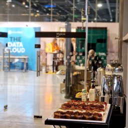 Chefs Catering - Stół cateringowy z ciastami i napojami na tle przeszklonego wejścia z napisem 'Wyjście' i logo 'The Data Cloud'.