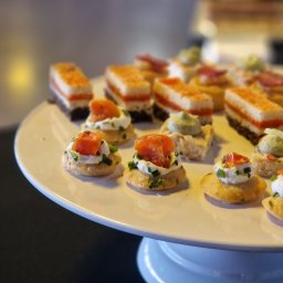 Chefs Catering - Różnorodne, apetyczne przekąski na białym, okrągłym paterze: krakersy z kremowym serem i łososiem, mini kanapeczki z pastami i wędlinami, ustawione w równych rzędach.