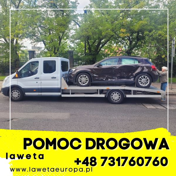 Uszkodzony brązowy samochód osobowy załadowany na białą platformę holowniczą na tle ulicy i zieleni, osoba starsza stoi obok pojazdu, w dolnej części zdjęcia widoczny żółty baner reklamowy...