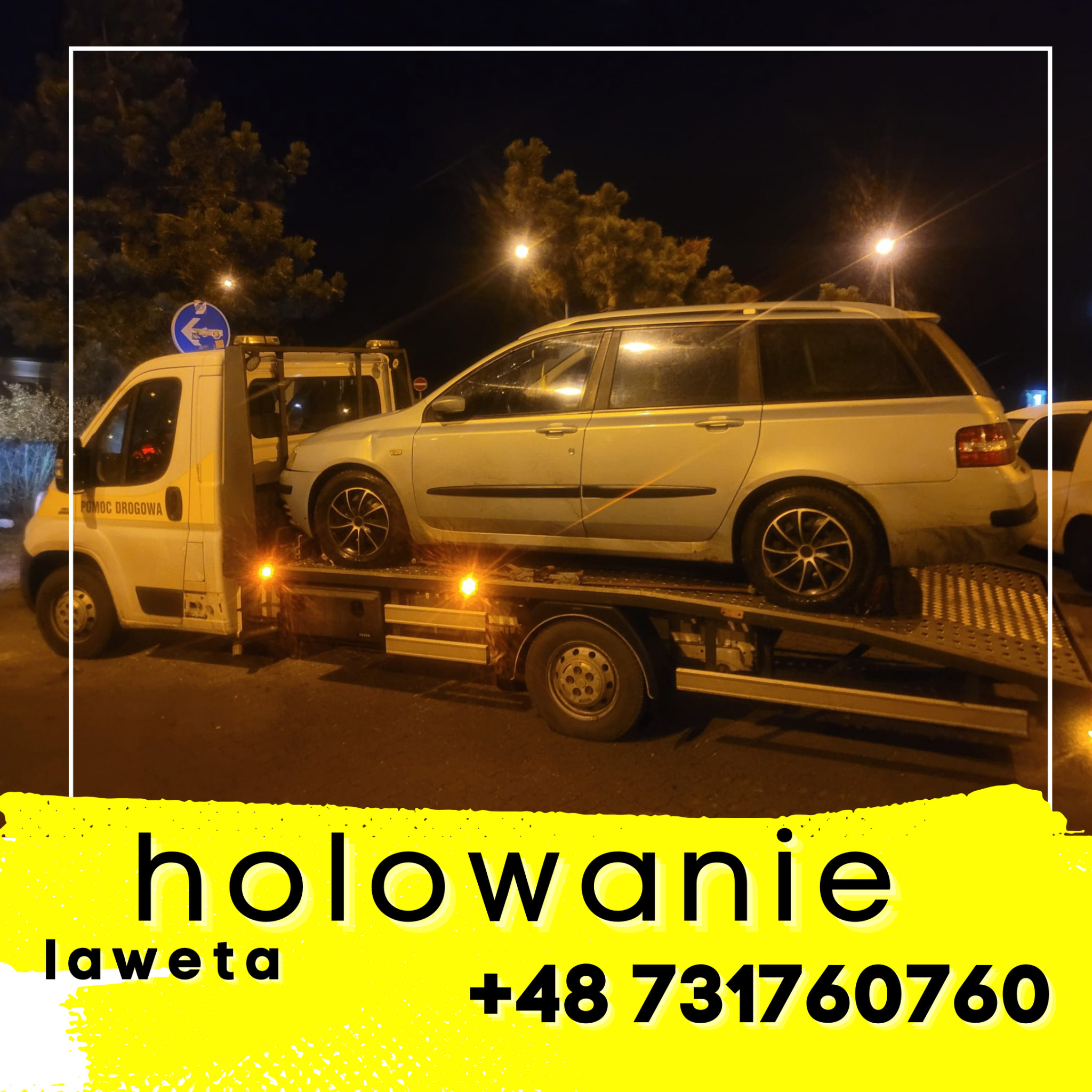 Samochód osobowy na platformie lawety pomocy drogowej w nocnej scenerii miejskiej.