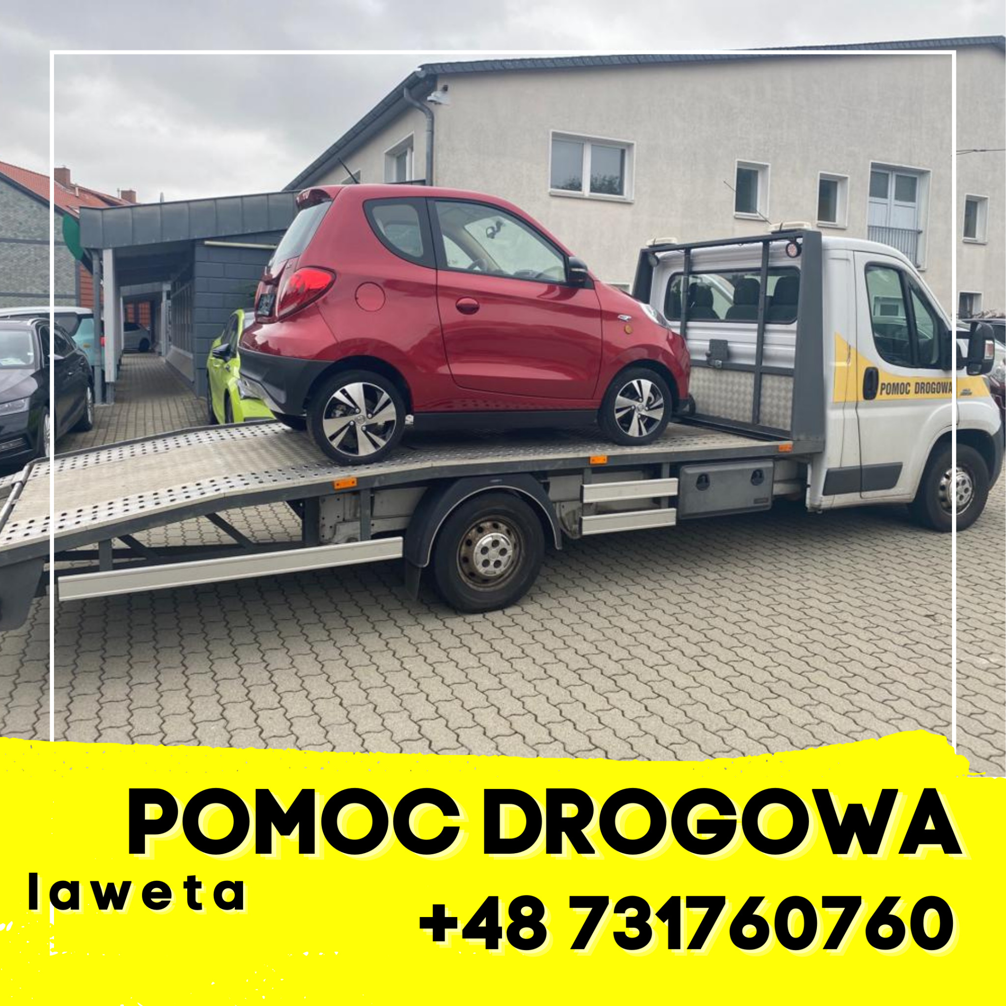 Czerwony samochód osobowy na platformie lawety pomocy drogowej, zaparkowanej na brukowanym placu przed budynkiem.