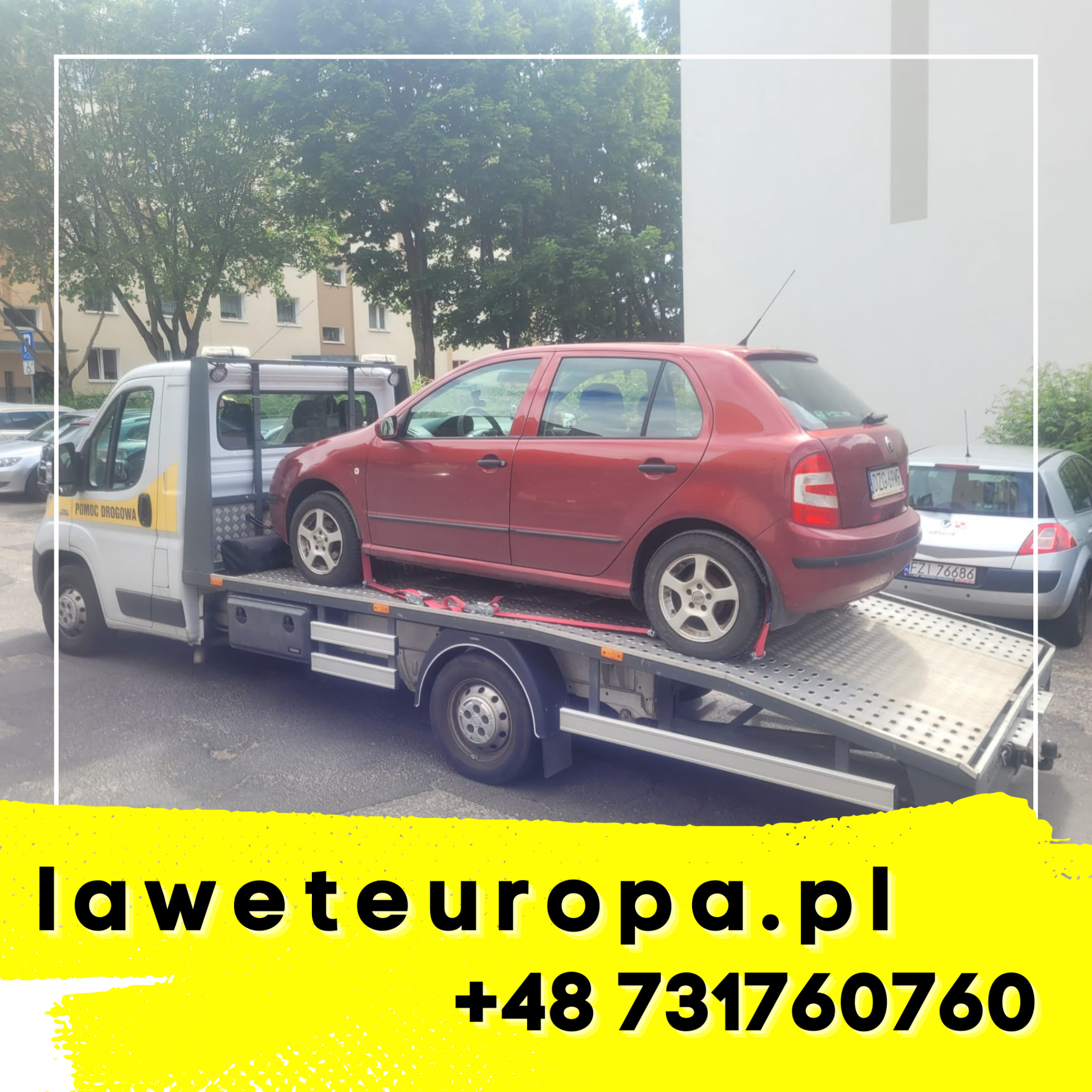 Czerwony samochód osobowy marki Skoda Fabia, zabezpieczony pasami, transportowany na platformie lawety pomocy drogowej na tle miejskiej ulicy z drzewami i budynkami.