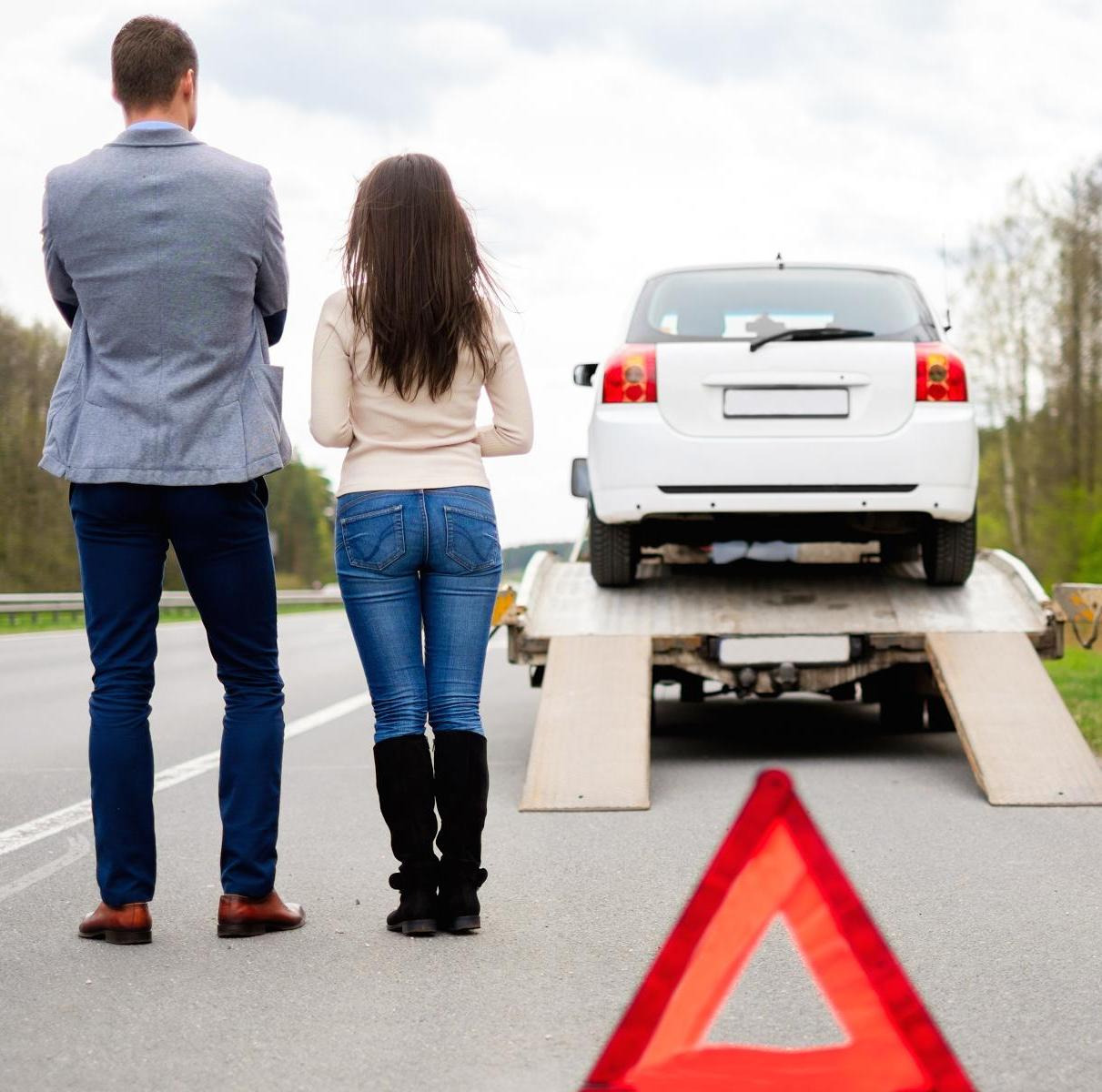 Para obserwuje biały samochód na lawecie na poboczu drogi, trójkąt ostrzegawczy na pierwszym planie.