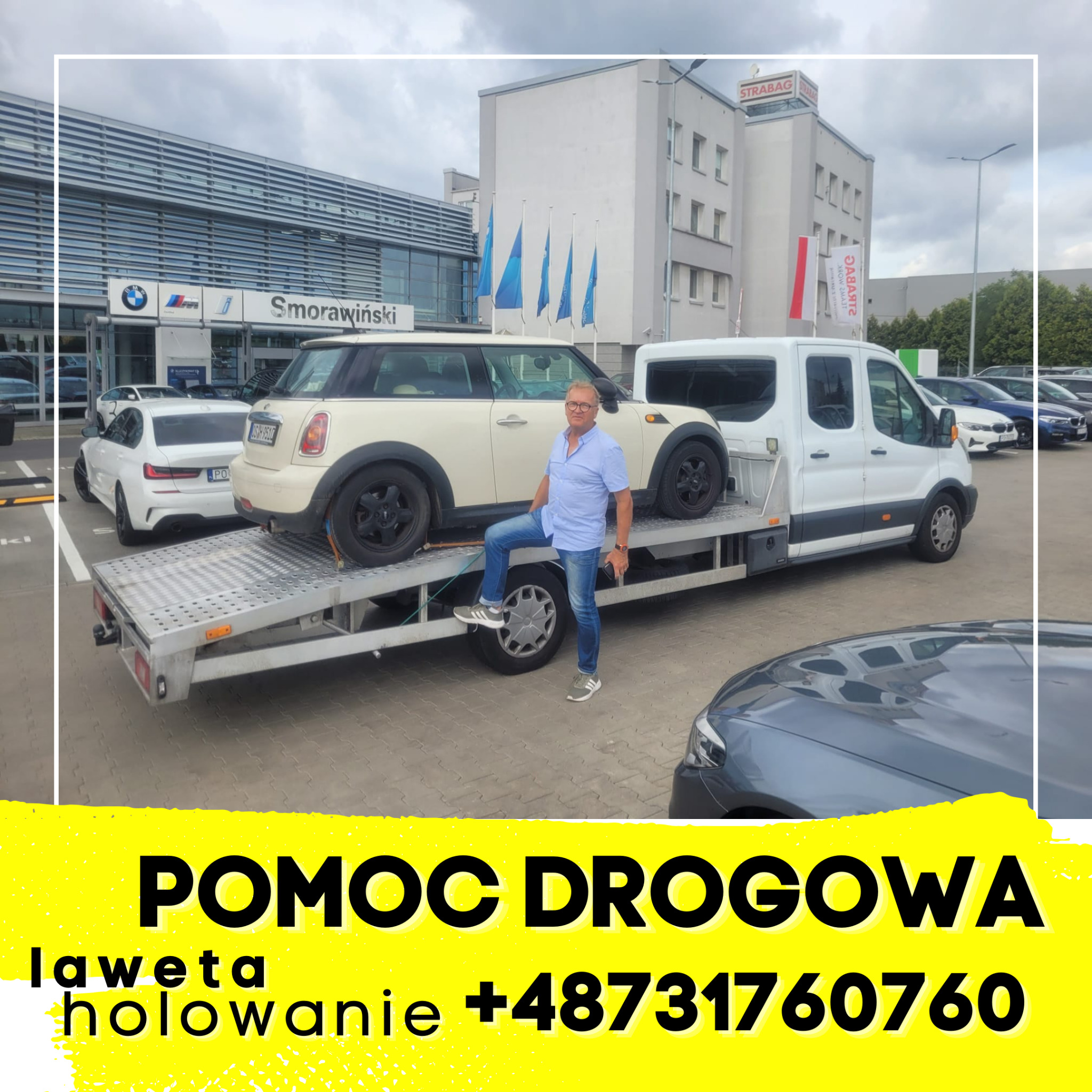Biała laweta z beżowym Mini Cooperem na platformie, mężczyzna w niebieskiej koszuli stoi na kole lawety, w tle salon BMW Smorawiński i budynek Strabag.