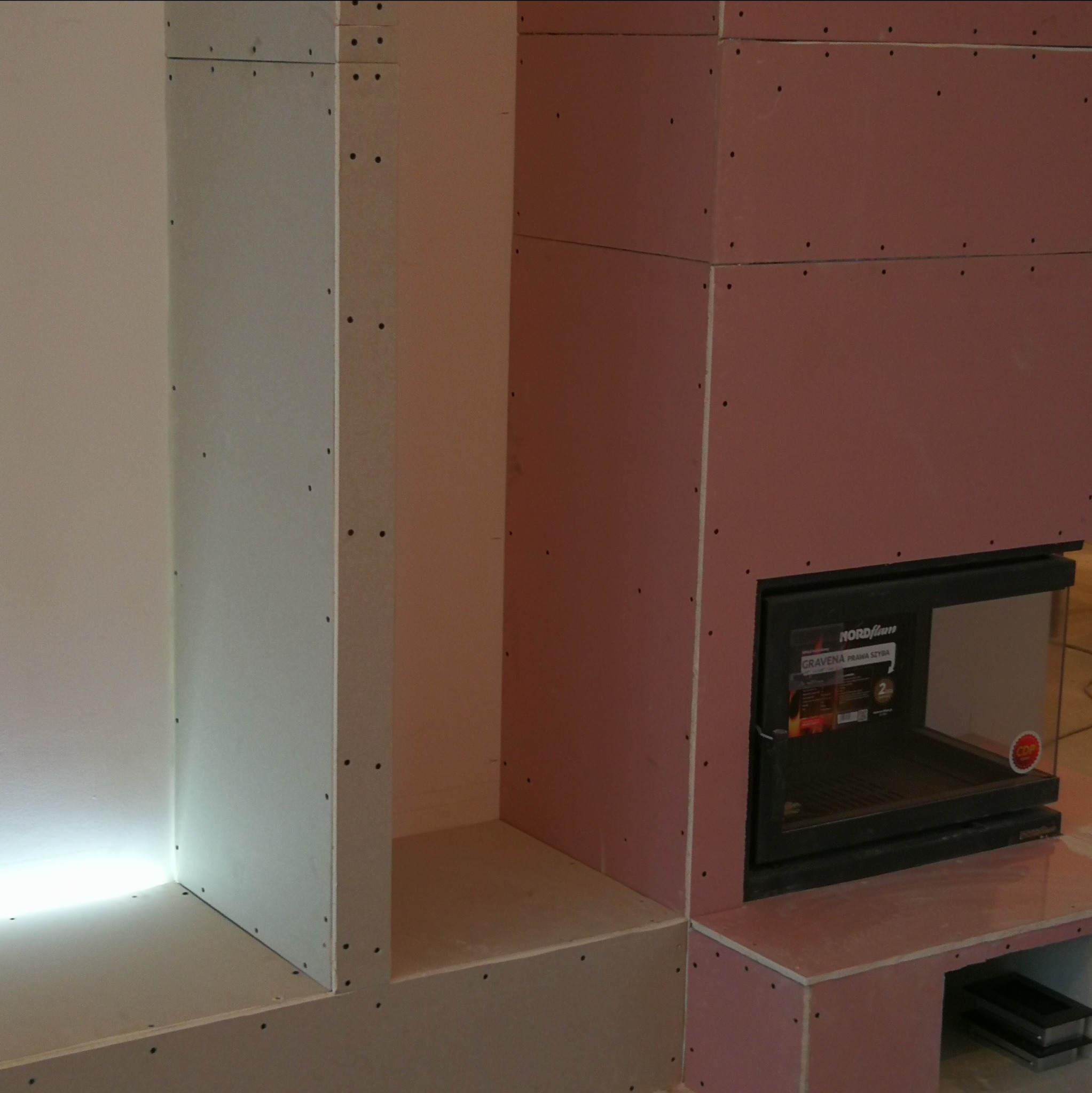 Konstrukcja obudowy kominka z płyt gipsowo-kartonowych, widoczne łączenia i wkręty, wbudowany wkład kominkowy Nordflam Gravena z prawą szybą.