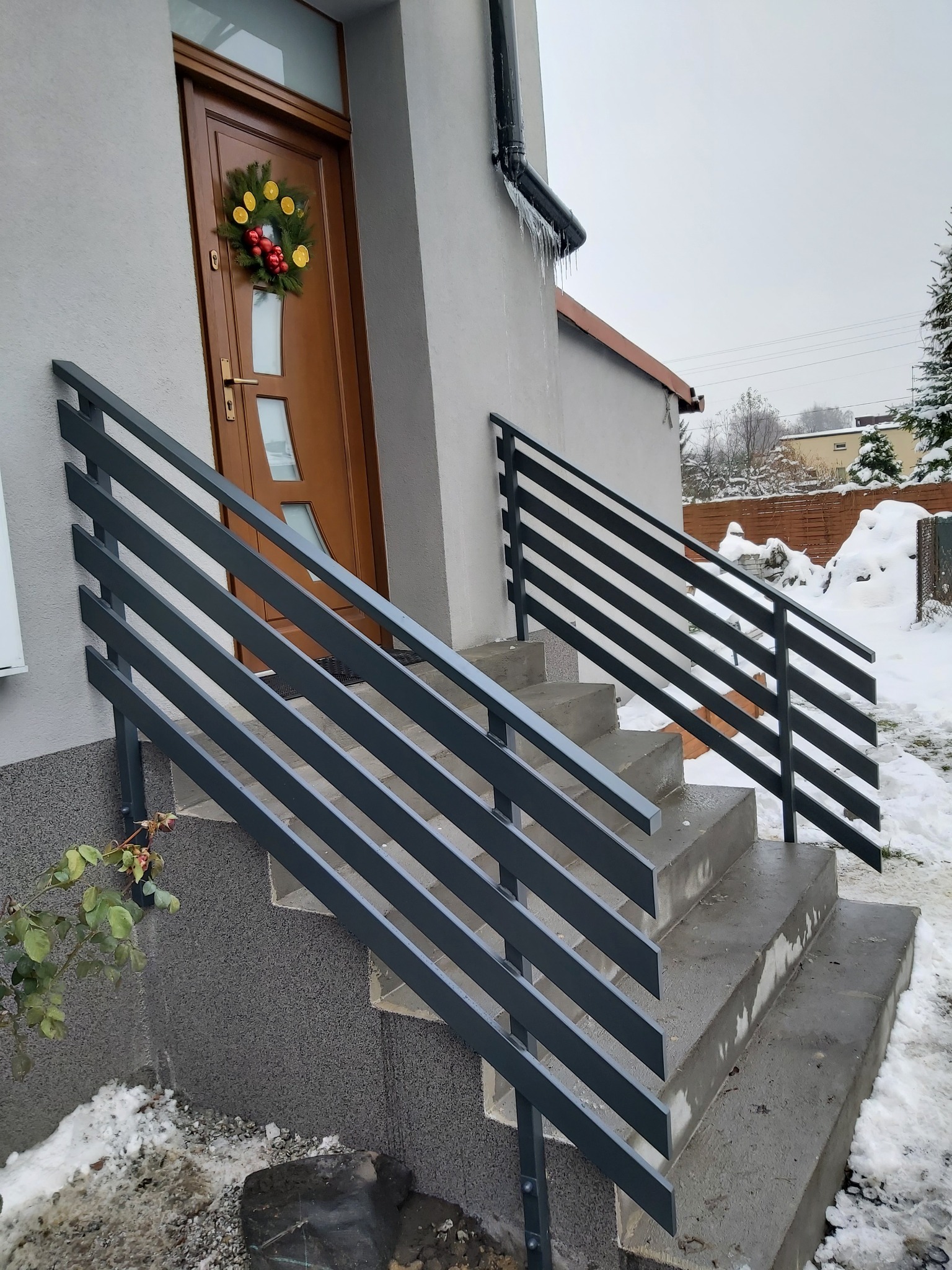 Nowoczesne, poziome, grafitowe barierki schodowe przed wejściem do domu, zimowa sceneria z śniegiem.